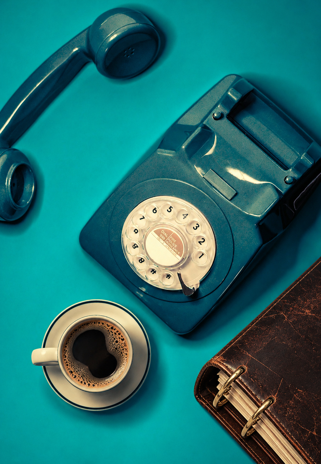 Teal rotary telephone beside a coffee and vintage notebook