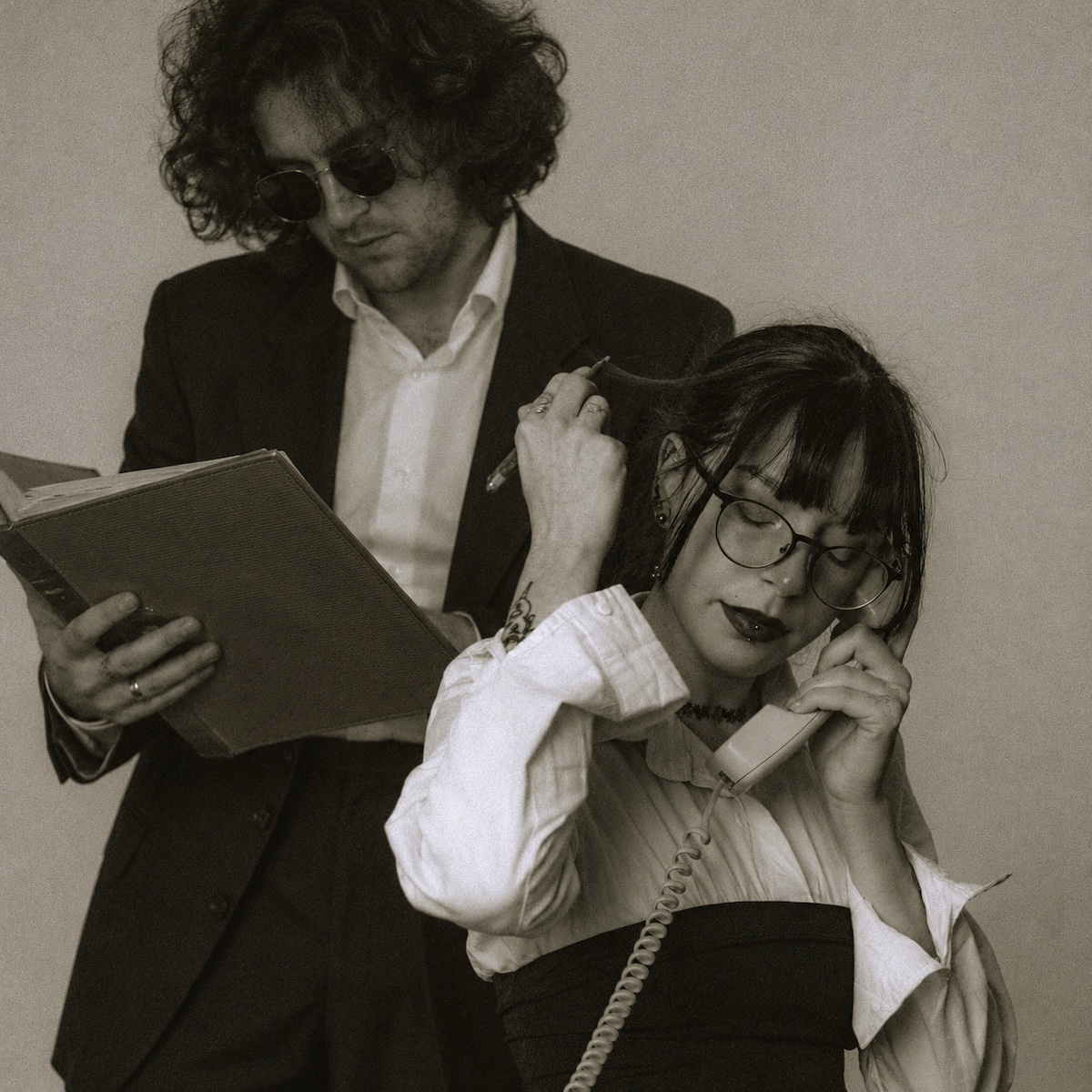 Two studio members, one on a retro phone and one reviewing a notebook