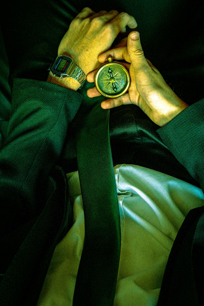 Hands holding a brass compass, a retro digital watch on the wrist